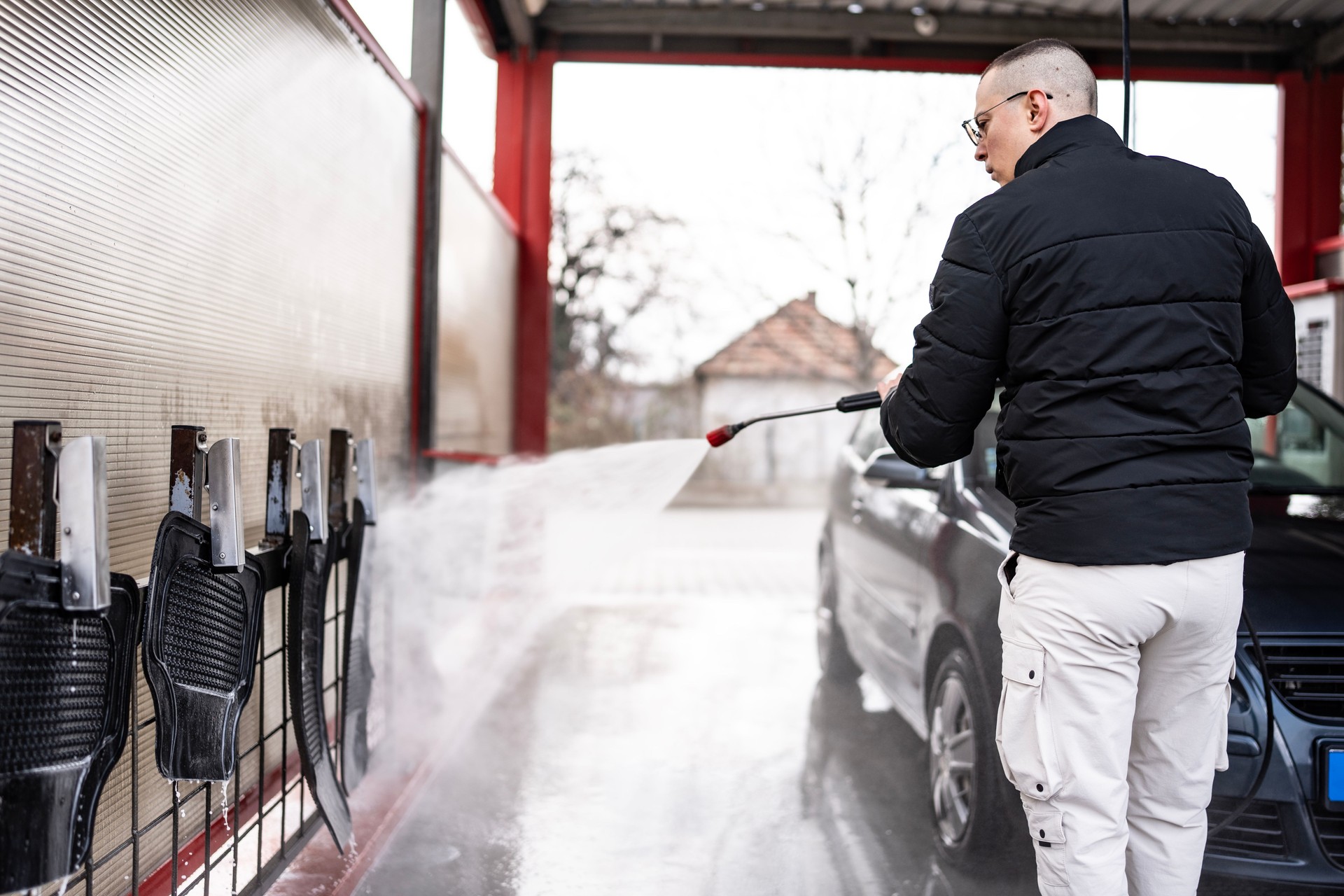 Man Cleaning a Car Using a Pressure Washer at an Outdoor Car Wash Station